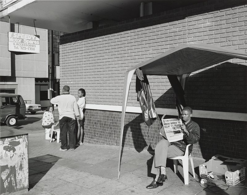A barber under his canopy and with a connection to electricity on Smit Street, Hillbrow, Johannesburg, 19 May 1999 by David Goldblatt