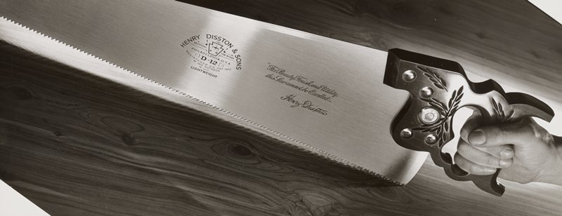 Hand holding Disston hand saw and sawing into wood plank, Edward W. Quigley, 1940