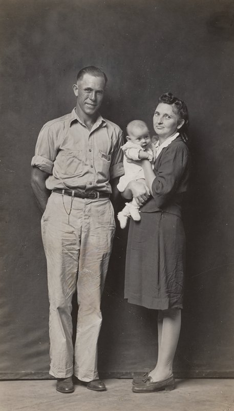 Standing father and mother holding baby by Mike Disfarmer