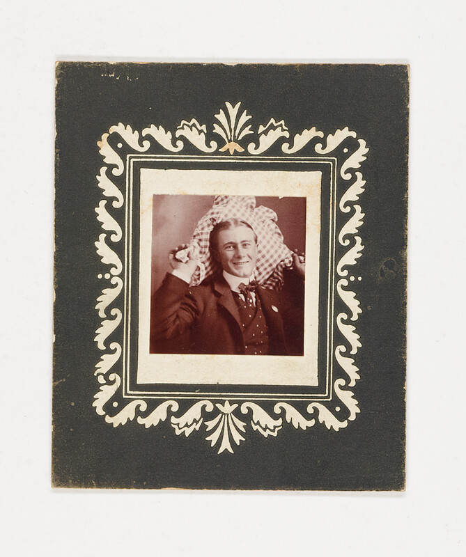 [Man posing with patterned pillow in decorative frame], c. 1910