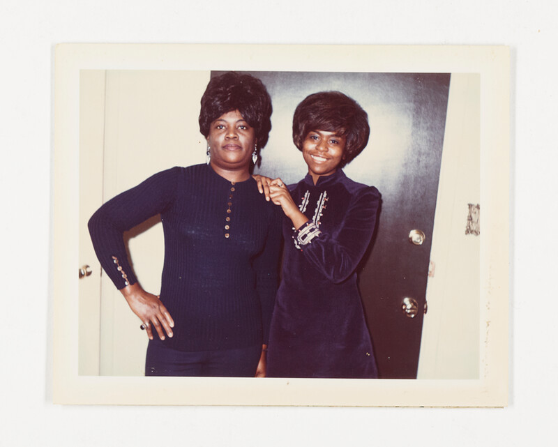 [Two women in dark dresses posing indoors], c. 1975
