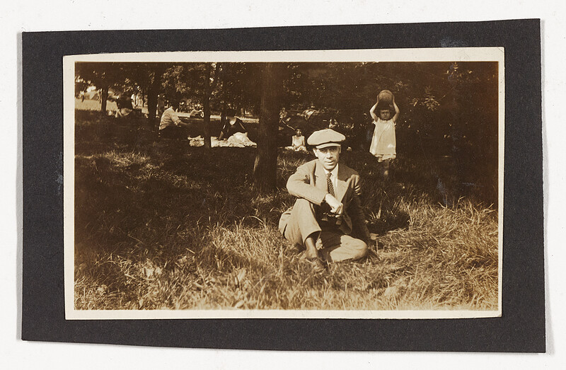[Man sitting on grass with child holding ball], c. 1920