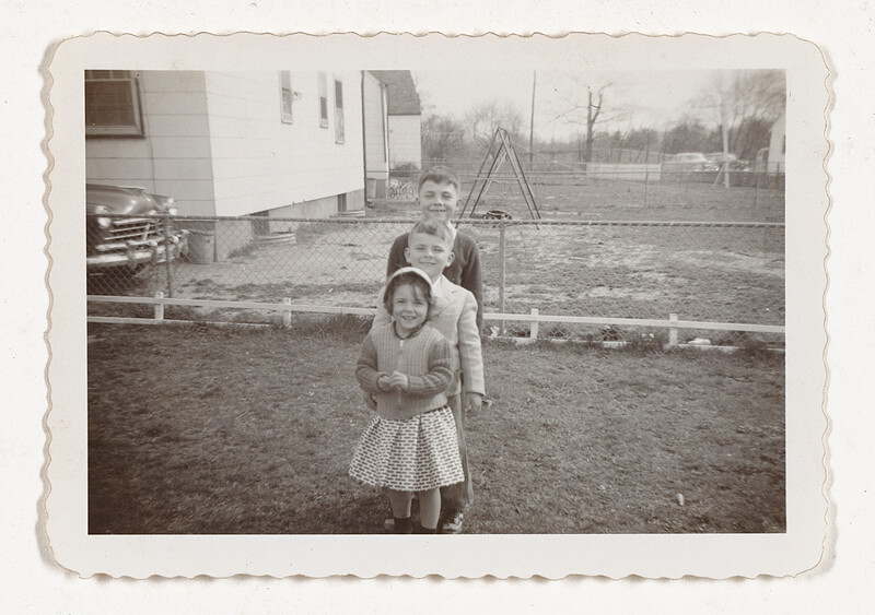 [Three children lined up outdoors, smiling], c. 1950–60