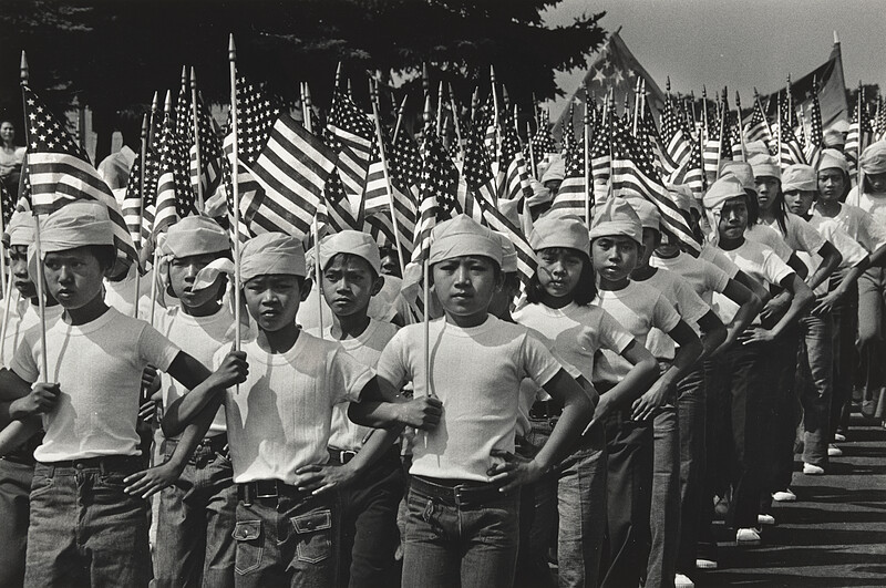 Barely two months after the fall of Saigon, U.N. refugee boys and girls march in a 4th of July parade organized by Americans at Indiantown Gap Refugee Camp, Pa., Charles Isaacs, 1975